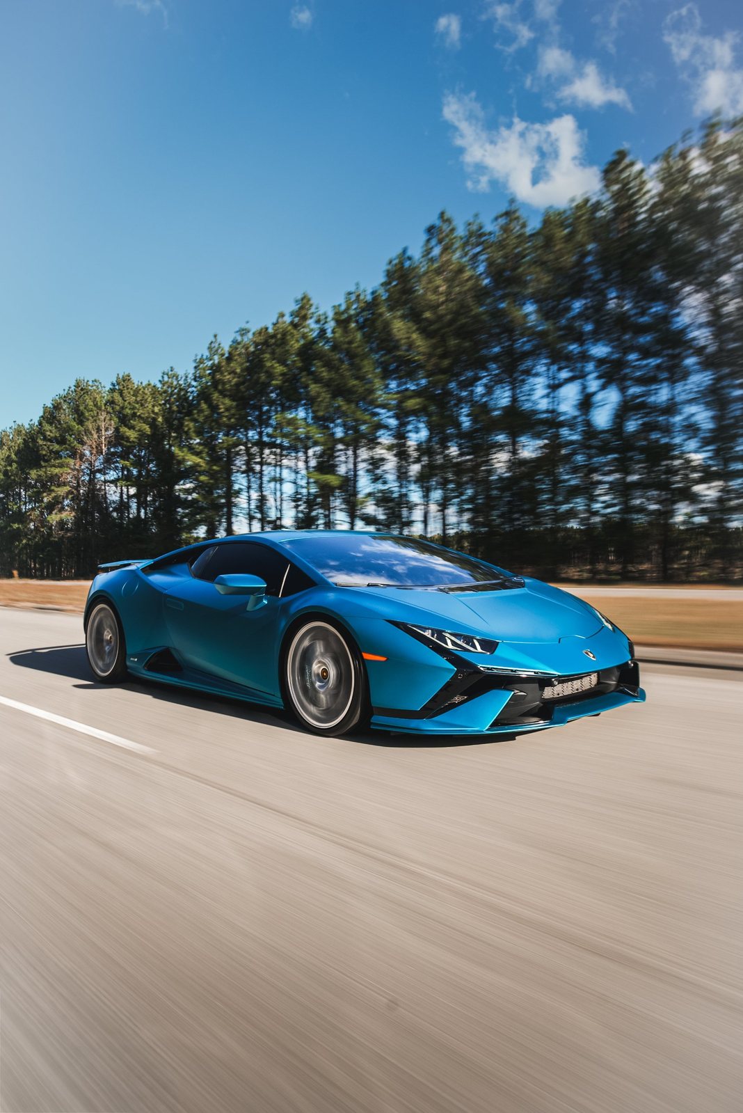 Blue Lamborghini Huracan Tecnica rolling shot on a tree-lined road