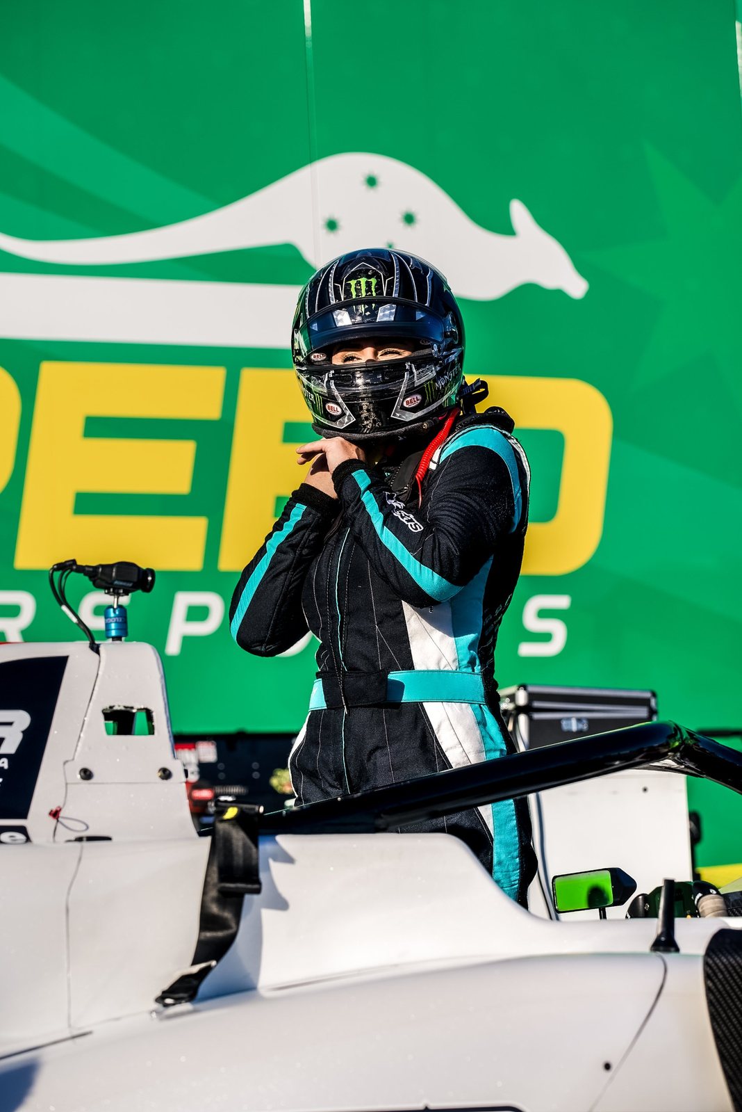 Driver in helmet and race suit standing beside a formula car