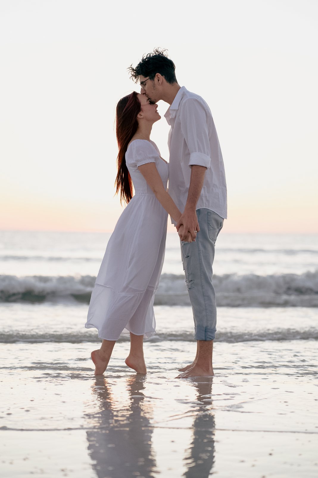 Couple sharing a forehead kiss in the surf at sunset