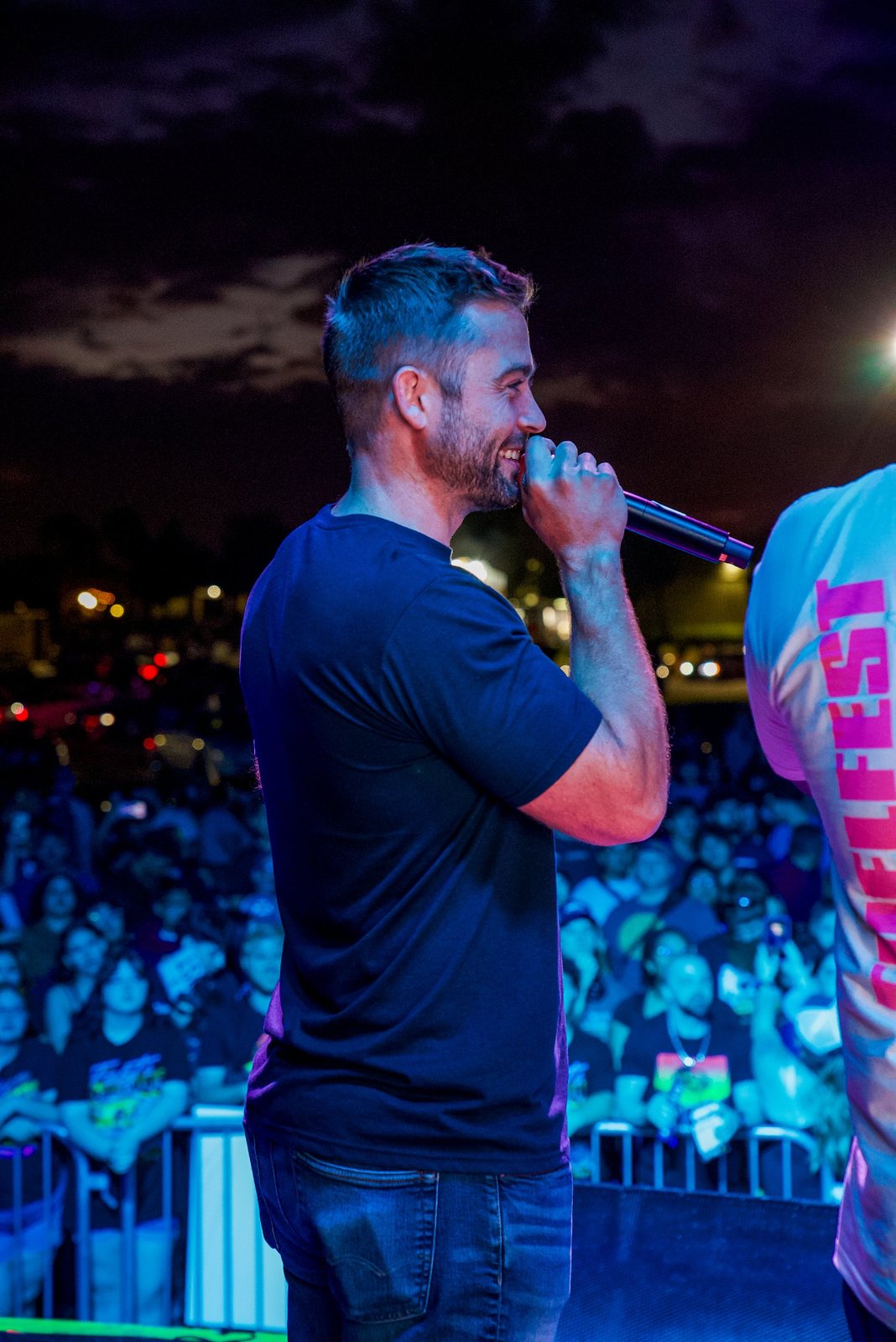 Speaker on stage with a microphone in front of a festival crowd