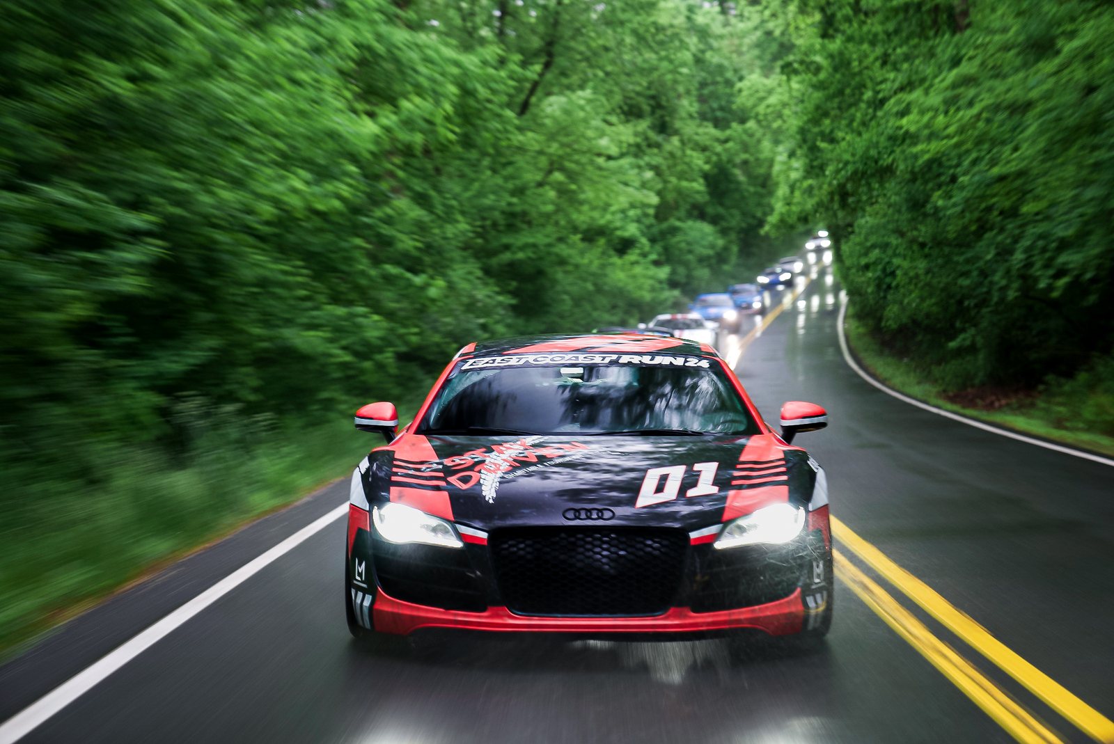 Audi R8 leading the East Coast Run convoy down a tree-lined road in the rain