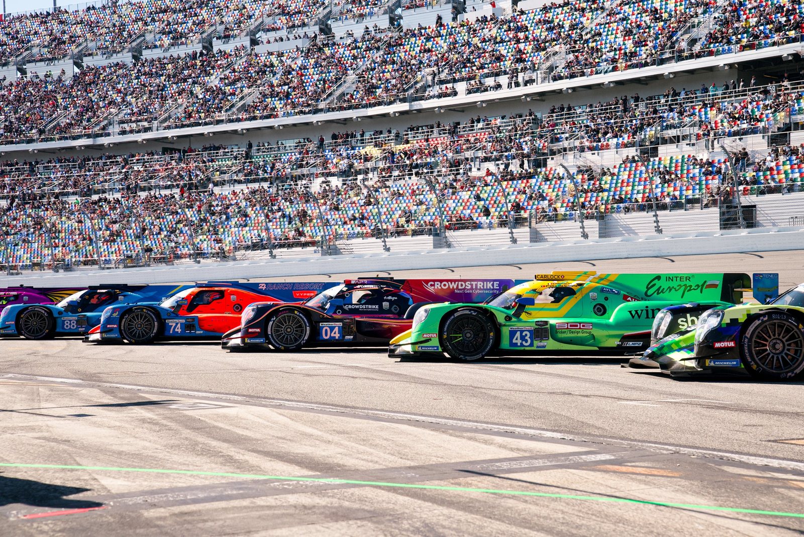 Prototype race cars lined up on the grid in front of packed grandstands at Daytona