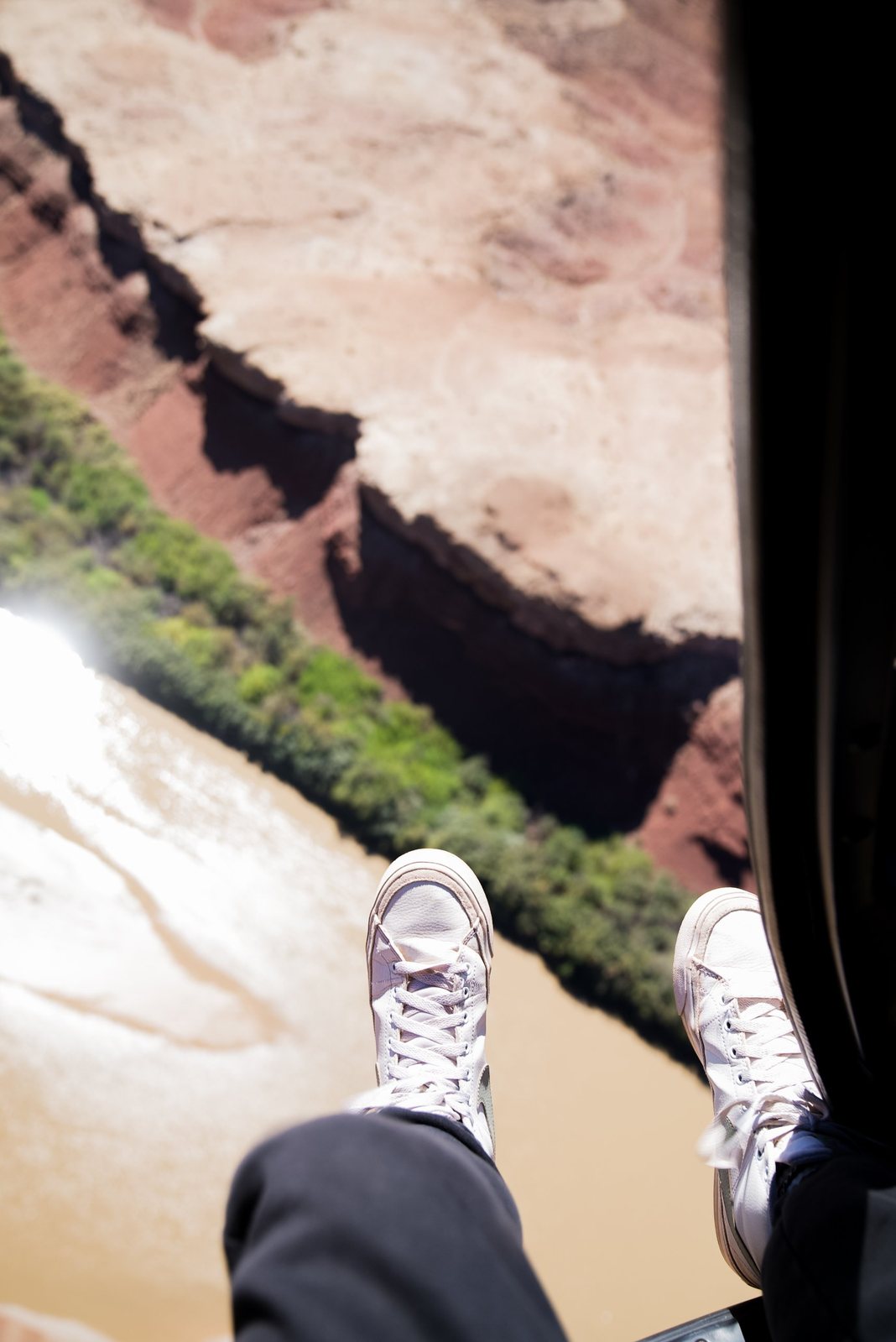 White sneakers dangling out of a helicopter over a red rock canyon and river