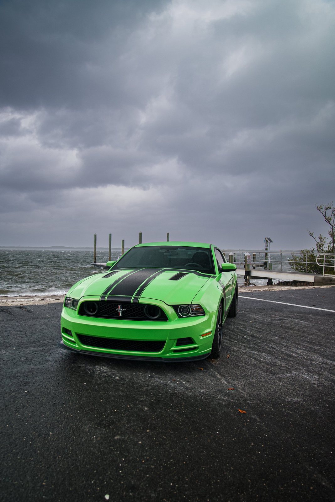 Green Mustang Boss 302 on a waterfront ramp under storm clouds
