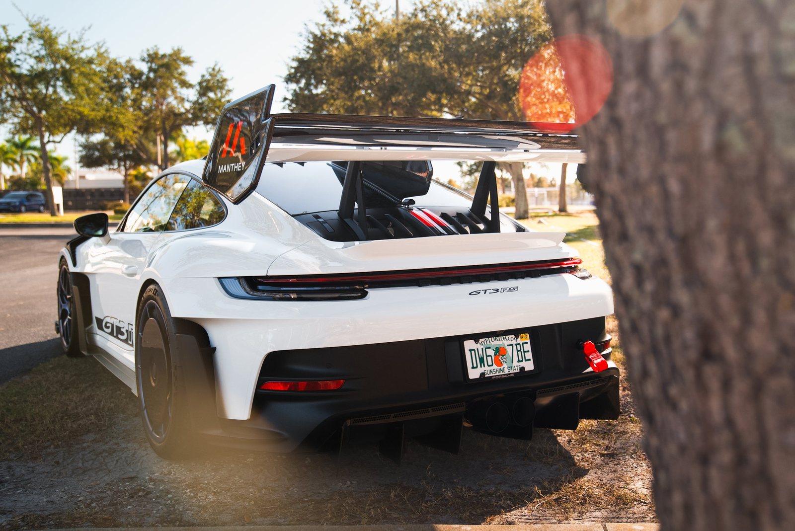 White Porsche GT3 RS with Manthey wing parked under the trees