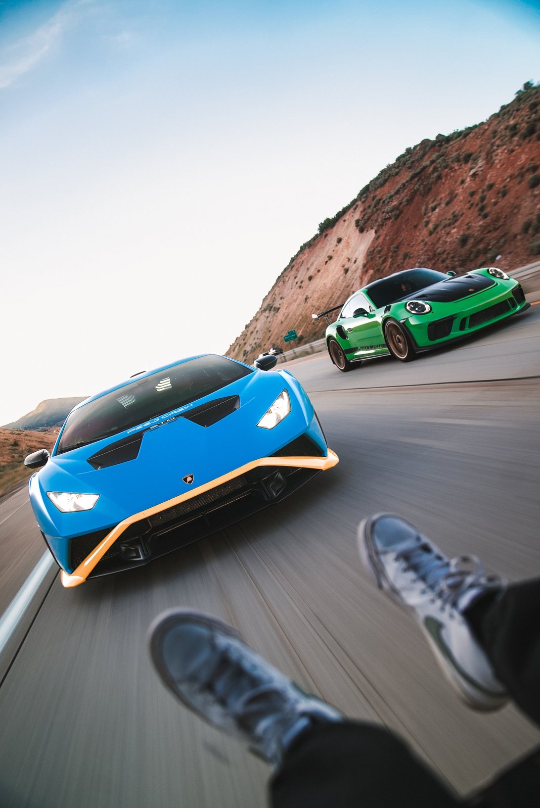 Blue Lamborghini Huracan STO and green GT3 RS on a canyon highway