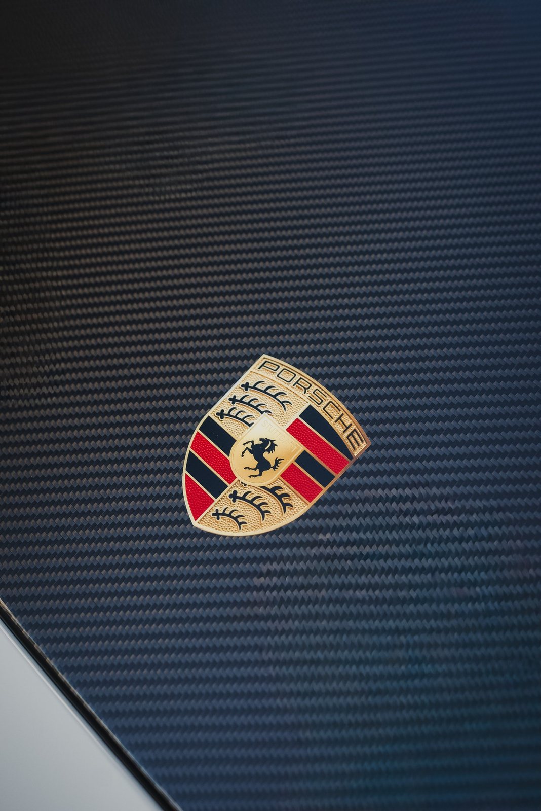 Gold Porsche crest on a carbon fiber hood