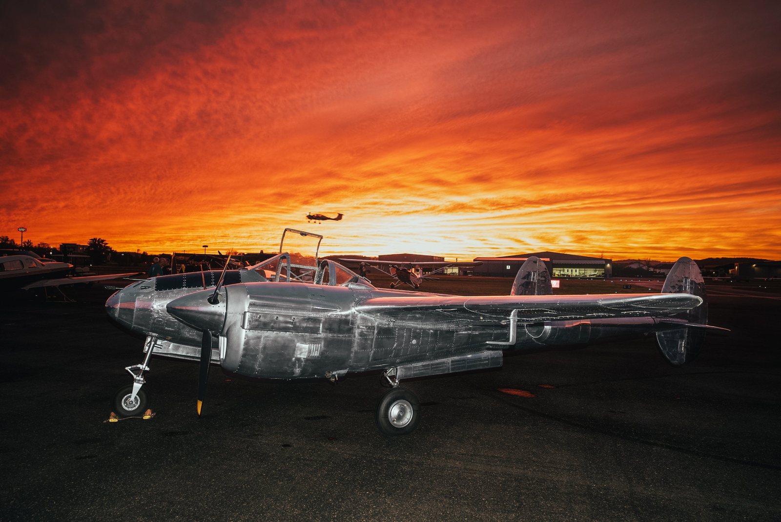 Polished P-38 Lightning on the ramp under a fiery orange sunset